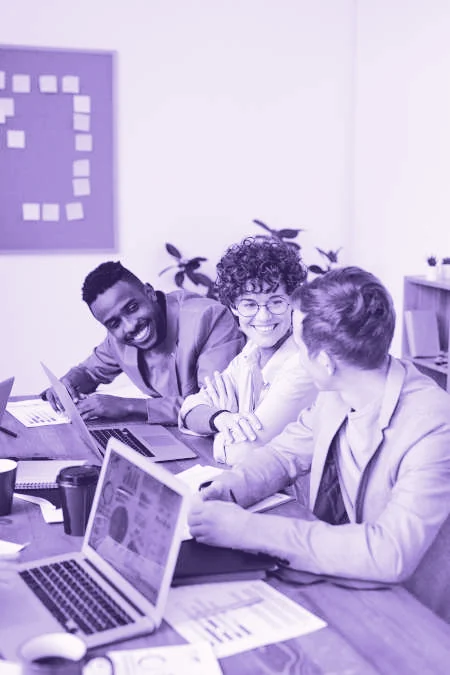 Equipo de trabajo conversando y sonriendo alrededor de una mesa con computadoras